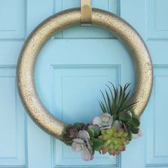 a gold wreath with succulents and plants hanging on a blue front door