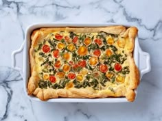 a casserole dish with tomatoes, spinach and cheese in it on a marble surface