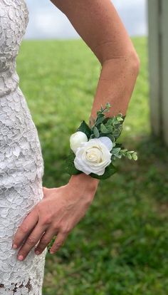 a woman wearing a white dress holding a flower in her left hand with grass and sky in the background