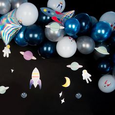 an assortment of balloons and space themed decorations on a black surface with stars, rockets, planets, and moon shapes