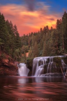 a waterfall in the middle of a forest at sunset