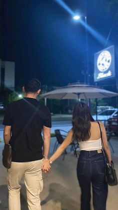 a man and woman holding hands while standing in front of an outdoor area at night