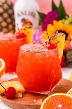 two glasses filled with orange juice and garnished with cherries on a cutting board