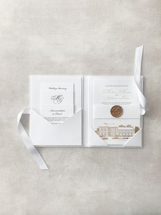 an open pocketfold wedding card with a white ribbon and a gold coin on it