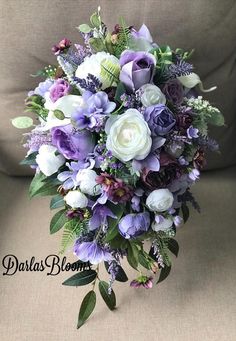 a bridal bouquet with purple and white flowers on a couch in front of a pillow