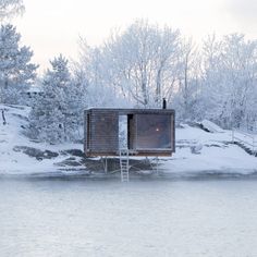 a small cabin sitting on top of a snow covered hillside next to a body of water