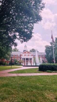 a large building with a fountain in front of it and trees around the perimeter, on a sunny day