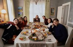 a group of people sitting around a dinner table with food on the dining room table