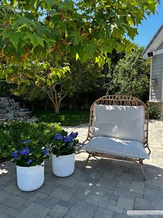 two white planters with blue flowers in them sitting on a patio next to a chair