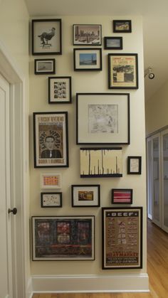 a wall with many framed pictures on it and wooden floors in front of the door