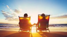 two people sitting in lawn chairs on the beach facing the ocean at sunset or sunrise