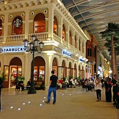 people are walking around in the lobby of a shopping mall with lights on and palm trees