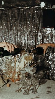 two people are pouring champagne into wine glasses on a table with silver sequins