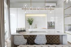 a white kitchen with two chairs and a bar in the middle, surrounded by wine bottles