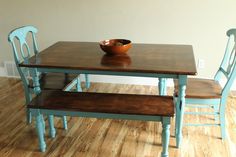 a wooden table with two blue chairs and a bowl on top of it in front of a white wall