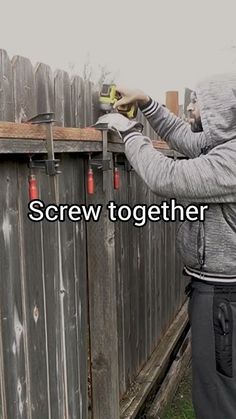 a man in a hoodie is using a power drill to screw holes on a fence