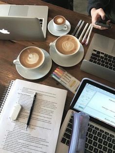 there are two cups of coffee on the table next to an open book and laptop