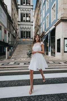 a woman standing in the middle of a crosswalk wearing a white dress and heels