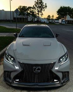 the front end of a silver car parked in a parking lot next to a street