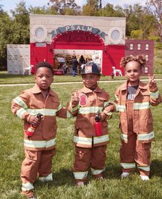 three young children dressed in fire fighter costumes posing for a photo with their hands up