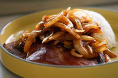 a yellow plate topped with meat covered in gravy and onions on top of rice