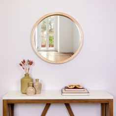 a mirror on the wall above a table with books and vases next to it