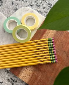 several pencils and tape sitting on top of a wooden board next to a plant