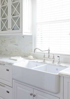 a kitchen with white cabinets and marble counter tops, along with a large double sink