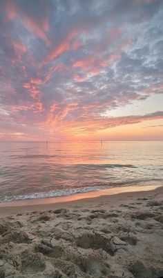 the sun is setting over the ocean with pink clouds in the sky and sand on the beach