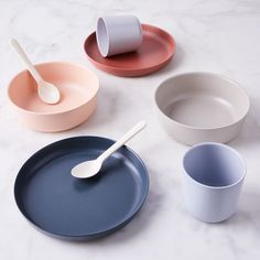 four different colored bowls and spoons on a marble table top with one empty cup