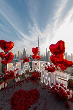 the word marry me is surrounded by red rose petals and balloons in the shape of hearts