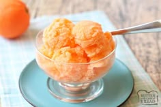 an orange ice cream in a small glass bowl on a blue plate with a spoon