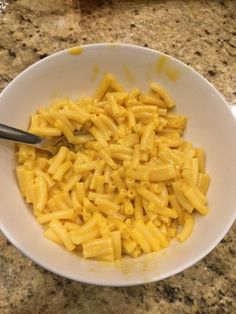 a white bowl filled with macaroni and cheese on top of a marble counter