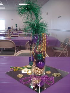 a purple table cloth topped with lots of beads and green plants in a tall glass vase