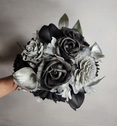 a bridal bouquet made with black and white flowers is being held by someone's hand