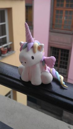 a small toy unicorn sitting on top of a black railing next to a pink building