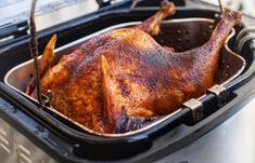 a roasting chicken in an air fryer with tongs sticking out of it