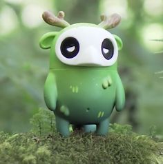 a small green toy with horns on it's head sitting in the grass next to some trees