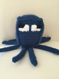 a crocheted blue octopus stuffed animal sitting on top of a white table next to a wall