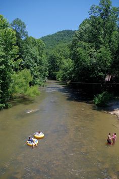 two people on rafts in the middle of a river surrounded by trees and hills