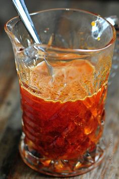 a glass filled with liquid sitting on top of a wooden table next to a spoon