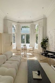 an elegant living room with white walls and flooring, along with large windows that look out onto the backyard