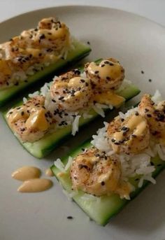 three pieces of cucumber with shrimp and rice on top, garnished with sesame seeds