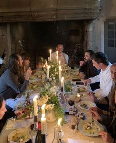 a group of people sitting around a table with food and candles on top of it