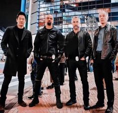 five men in leather jackets are standing on the sidewalk