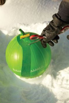 a person is holding scissors on top of an inflatable object with snow around it