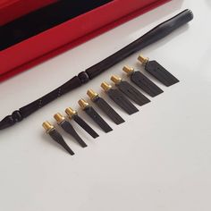 seven black and gold - plated knives are lined up next to a red box