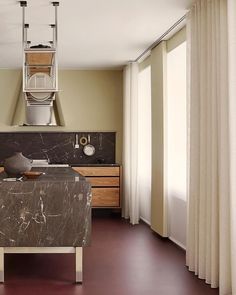 a kitchen with marble counter tops and wooden cabinets, along with white drapes on the windows