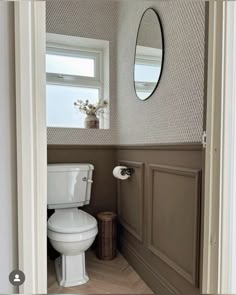 a white toilet sitting in a bathroom next to a window with a mirror above it