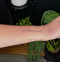 a person's arm with the word godupied tattooed on it, in front of a potted plant